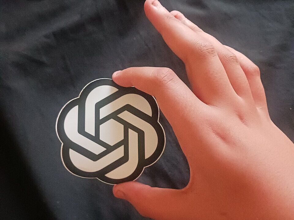 Hand holding an OpenAI logo sticker